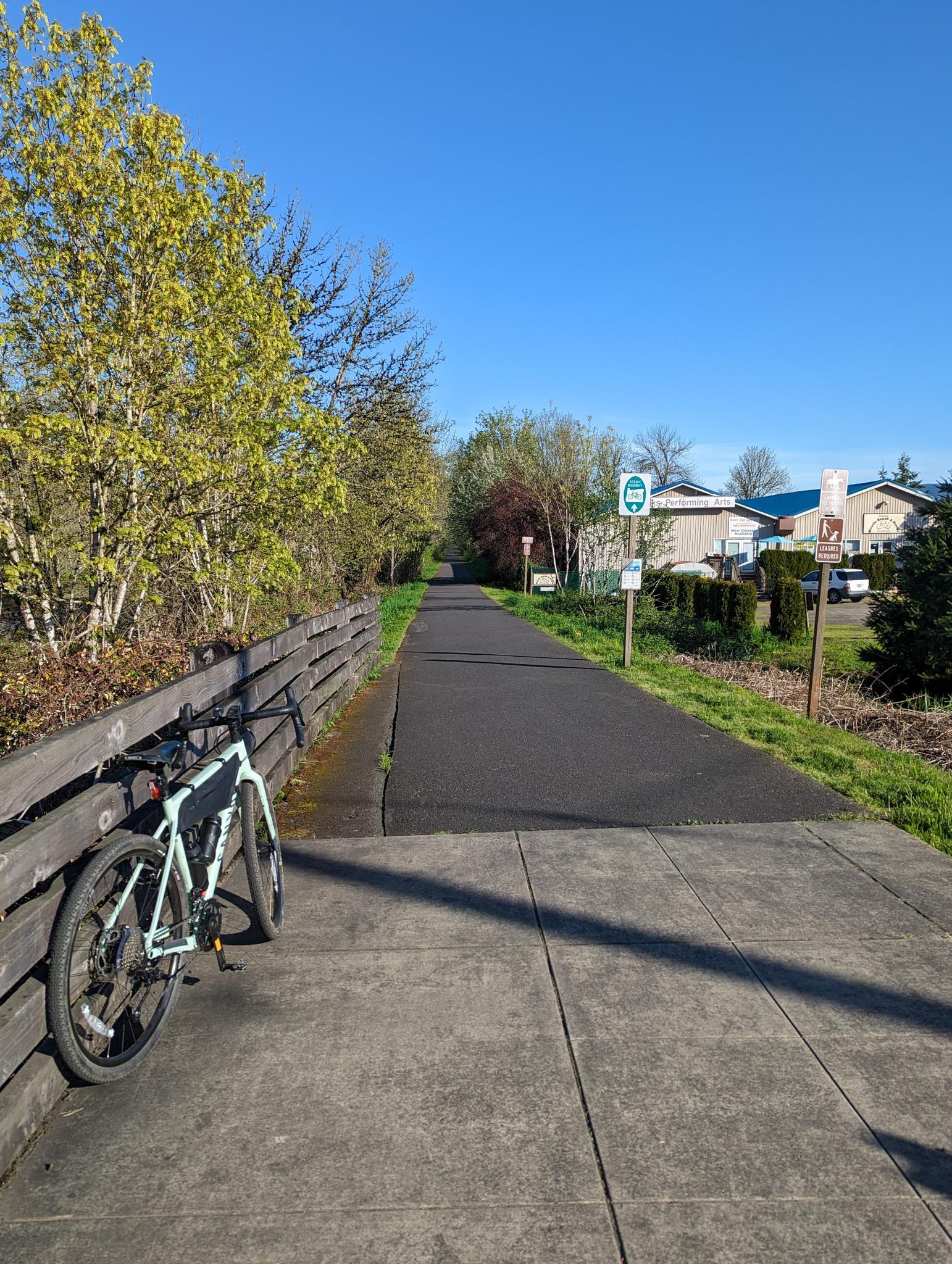 Paved path with a bicycle leaning on a fence under a clear blue sky.
