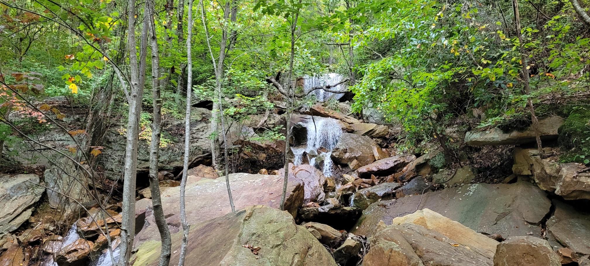 A multi-tiered waterfall flows over large rocks amidst a lush green forest.