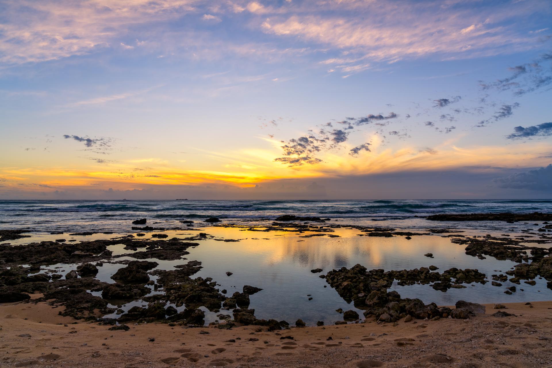 Rocky tidal pools reflecting a vibrant sunset sky over the ocean.