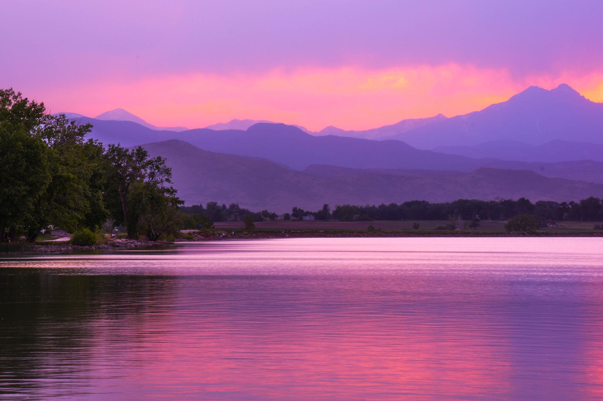 Vibrant purple and pink sunset over a calm lake with distant mountains.