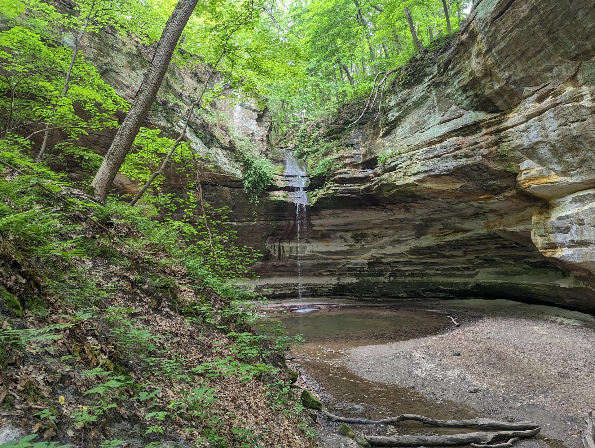 Small waterfall cascading into a pool within a rocky, green canyon.