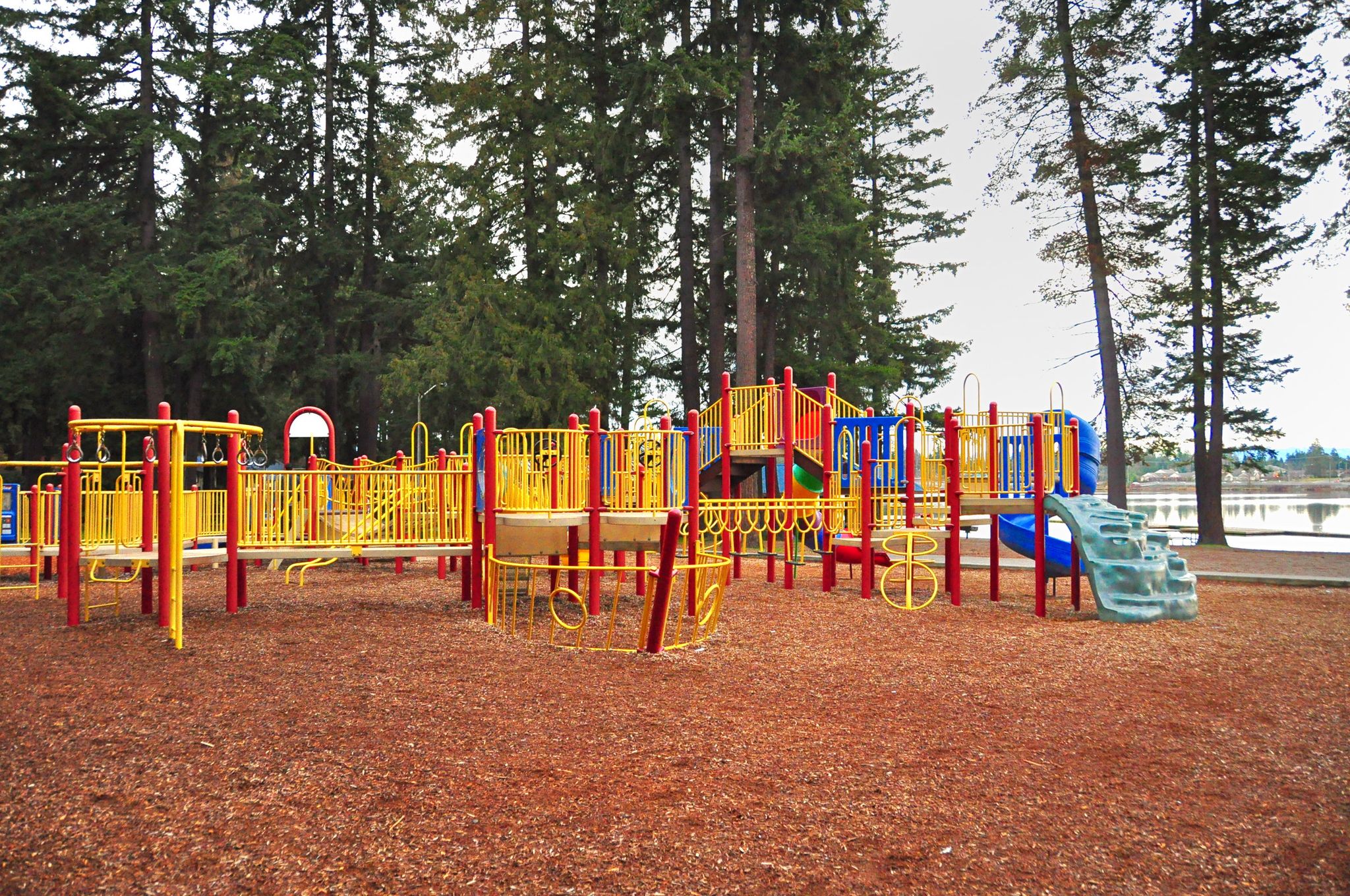 A colorful playground with slides and swings under tall evergreen trees. - Roadbike loop from Everett Station