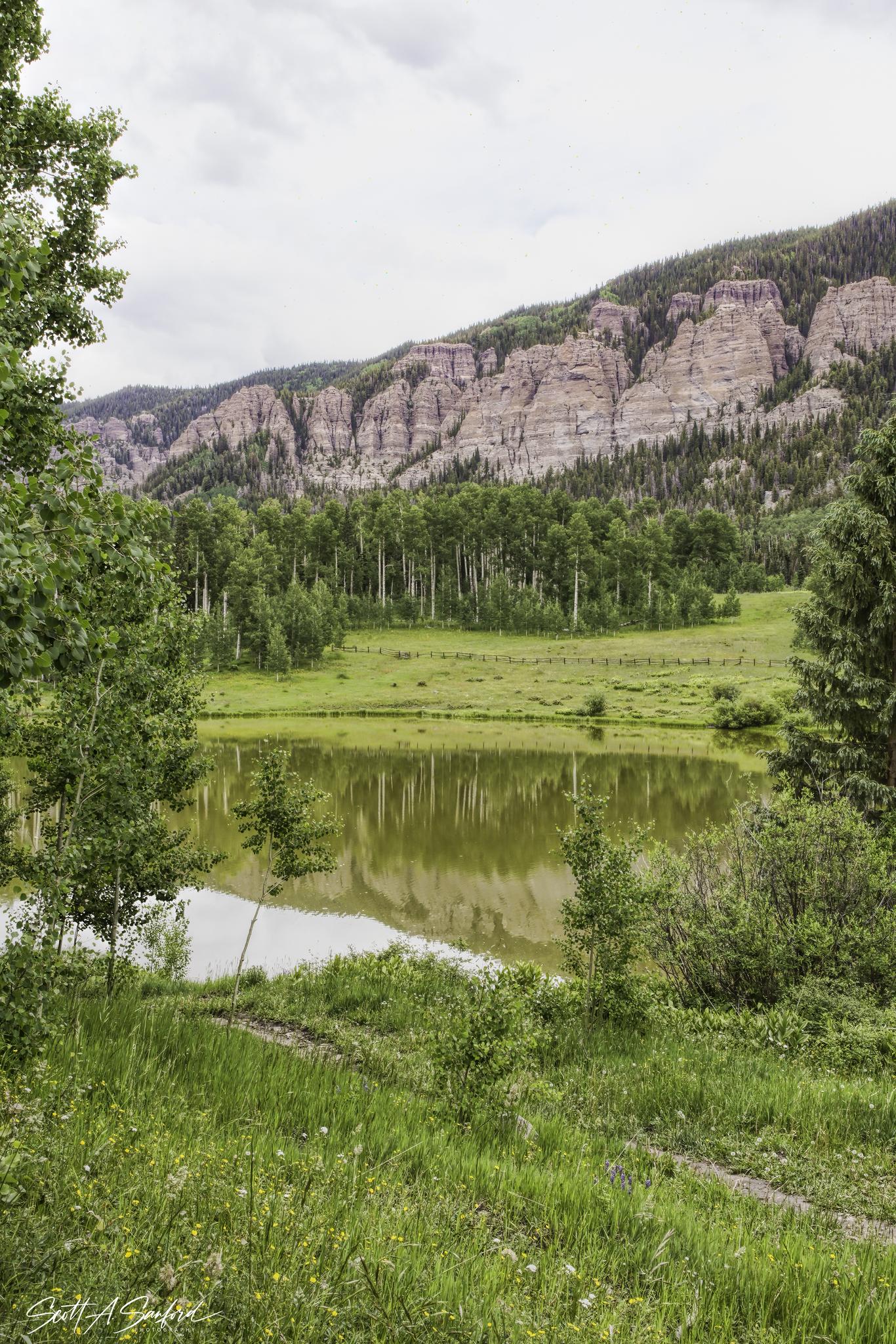 Serene lake reflecting rocky mountains and aspen trees under an overcast sky.