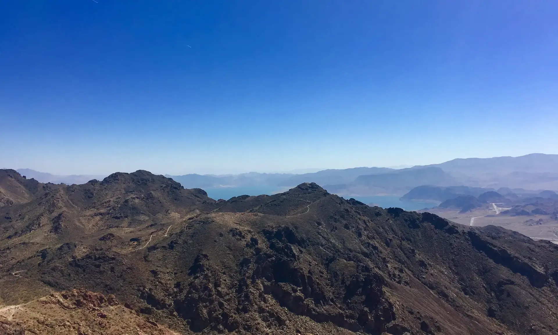 Expansive aerial view of rugged mountains, distant water, and clear blue sky.