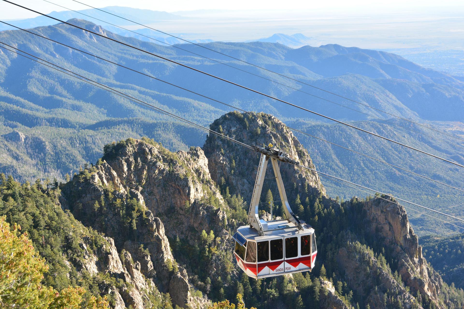 A cable car travels over a vast, rugged mountain landscape.