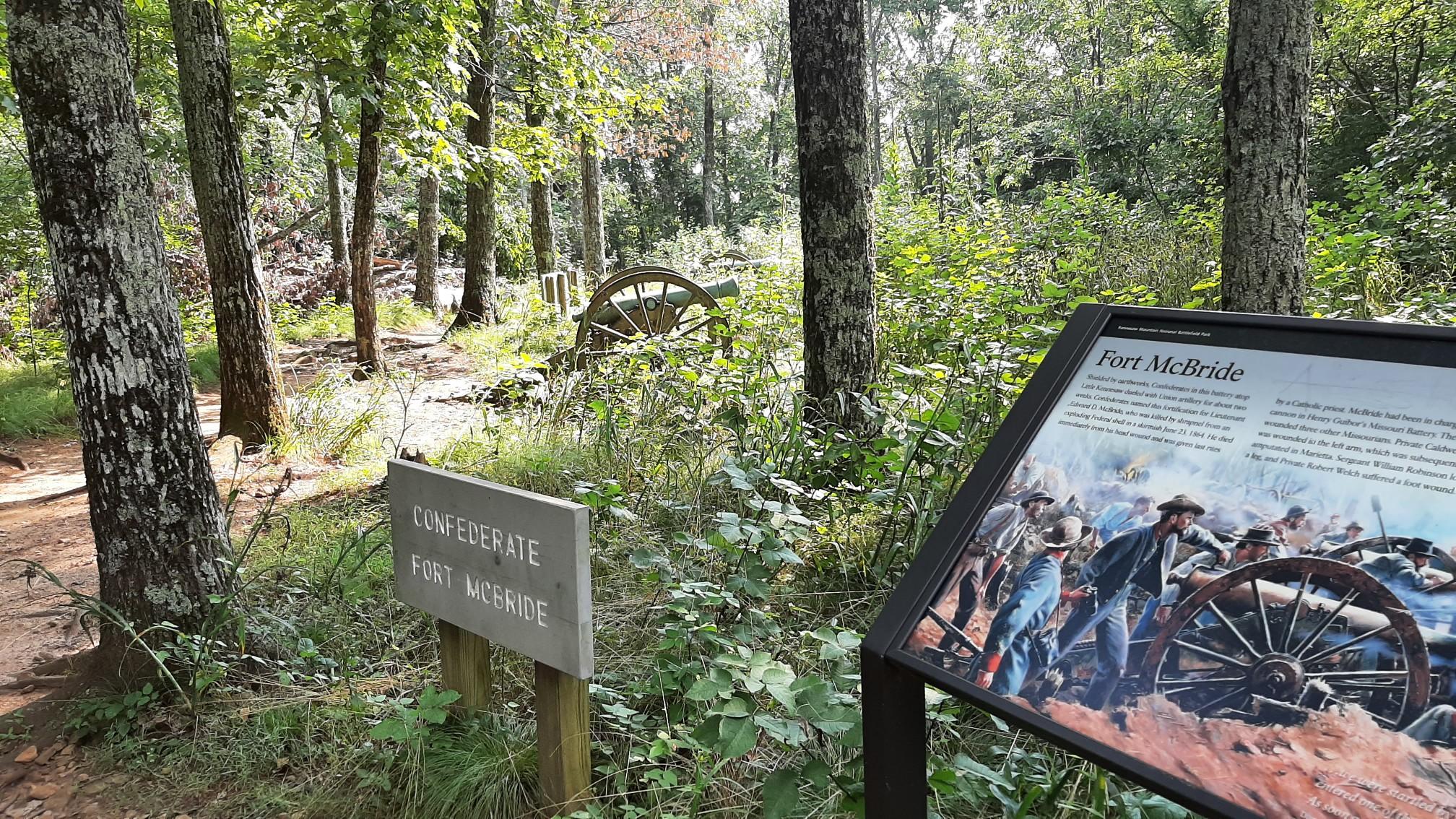Forest scene with historical signs, cannon wheels, and green foliage.