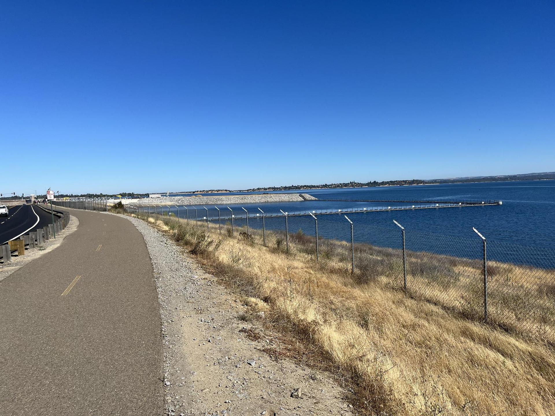 A paved path runs alongside a fence next to a large body of water.