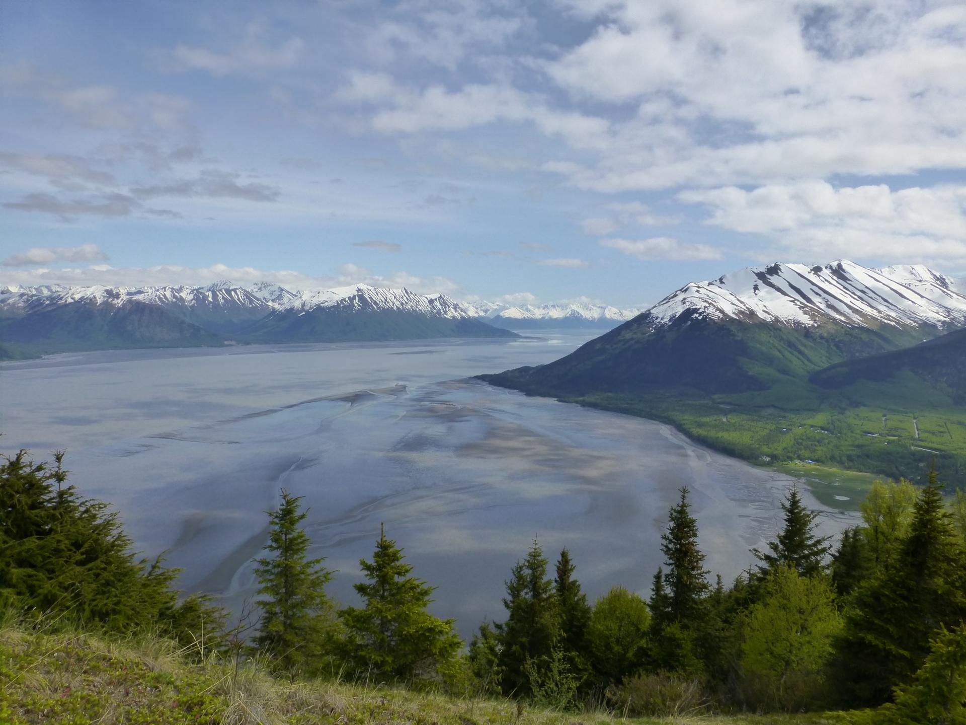 Panoramic view of a wide bay surrounded by snow-capped mountains under a cloudy sky.