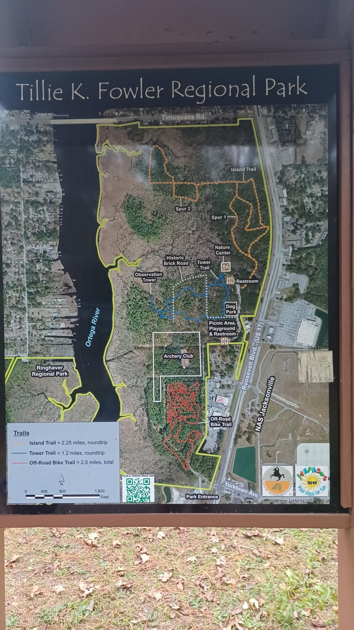An outdoor park map sign showing trails, a river, and wooded areas.
