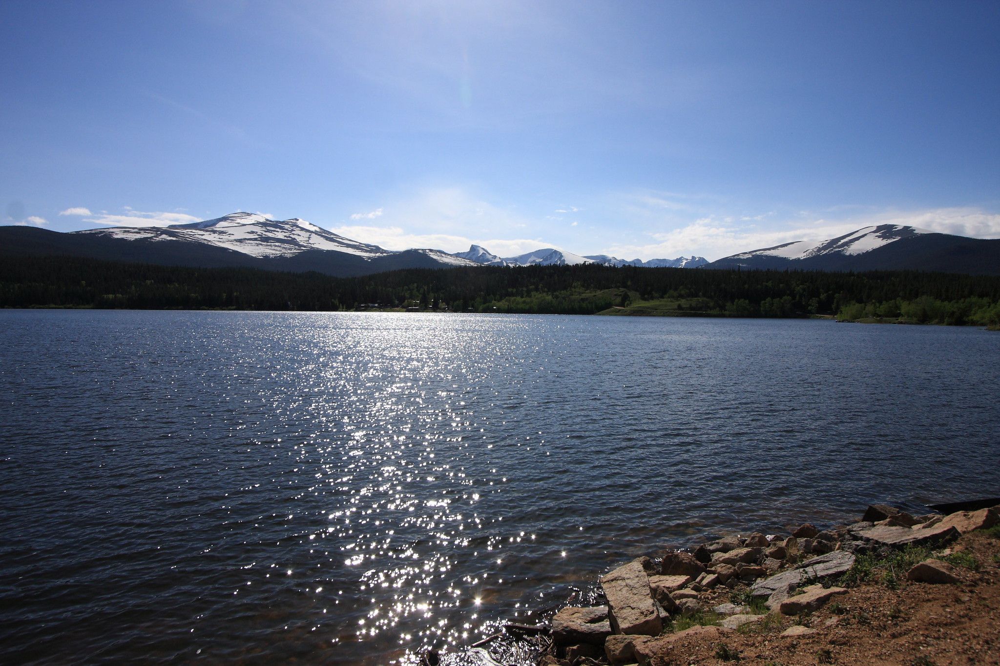 Sunlight glitters on a wide lake with snow-capped mountains and forest. - Coney Flats Trailhead – Beaver Reservoir and Trailhead loop from Beaver Reservoir Trailhead
