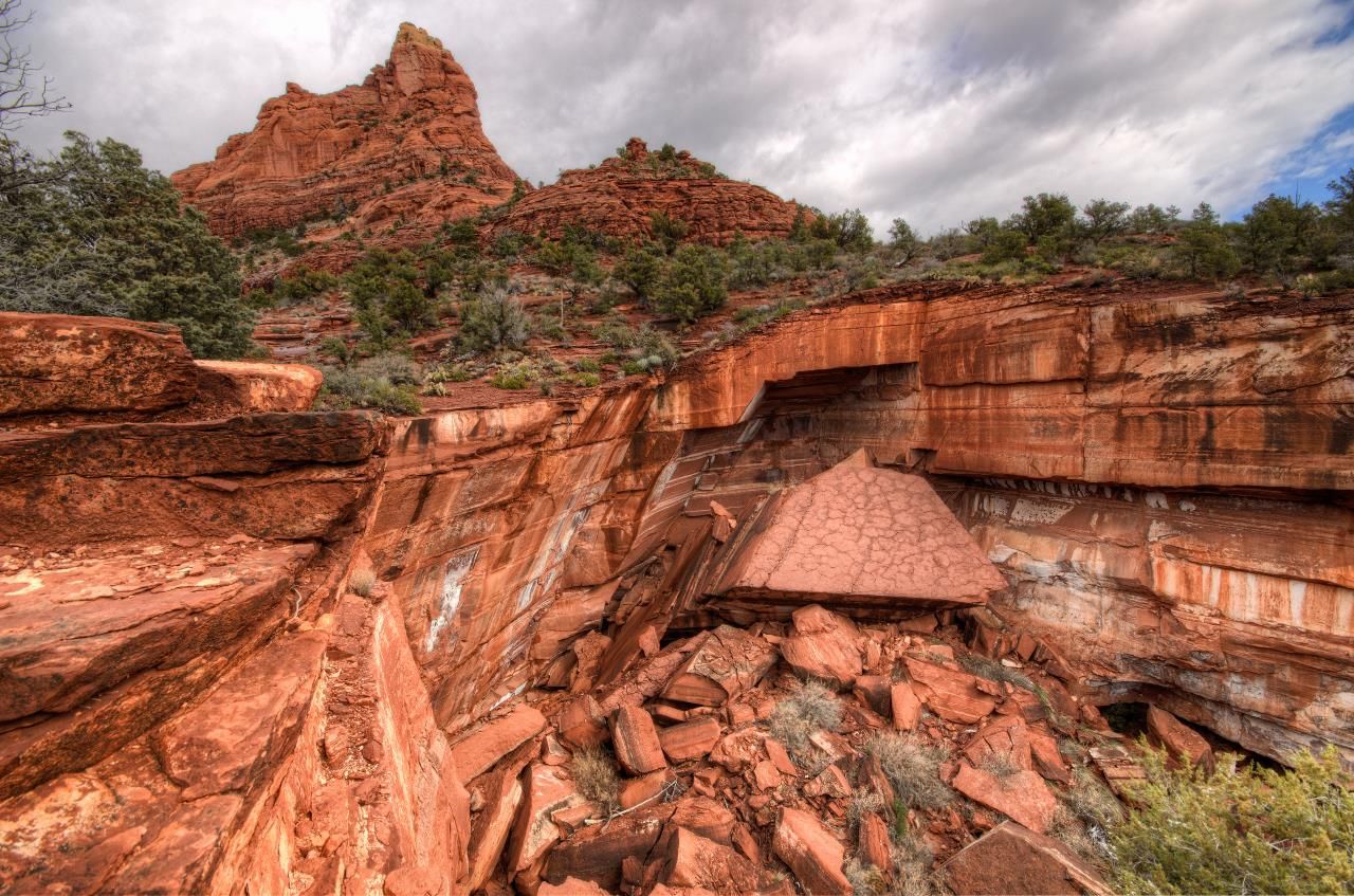 Dramatic red rock canyon with fallen boulders and green shrubs under a cloudy sky. - Soldier Pass & Brins Mesa loop – Red Rock-Secret Mountain Wilderness