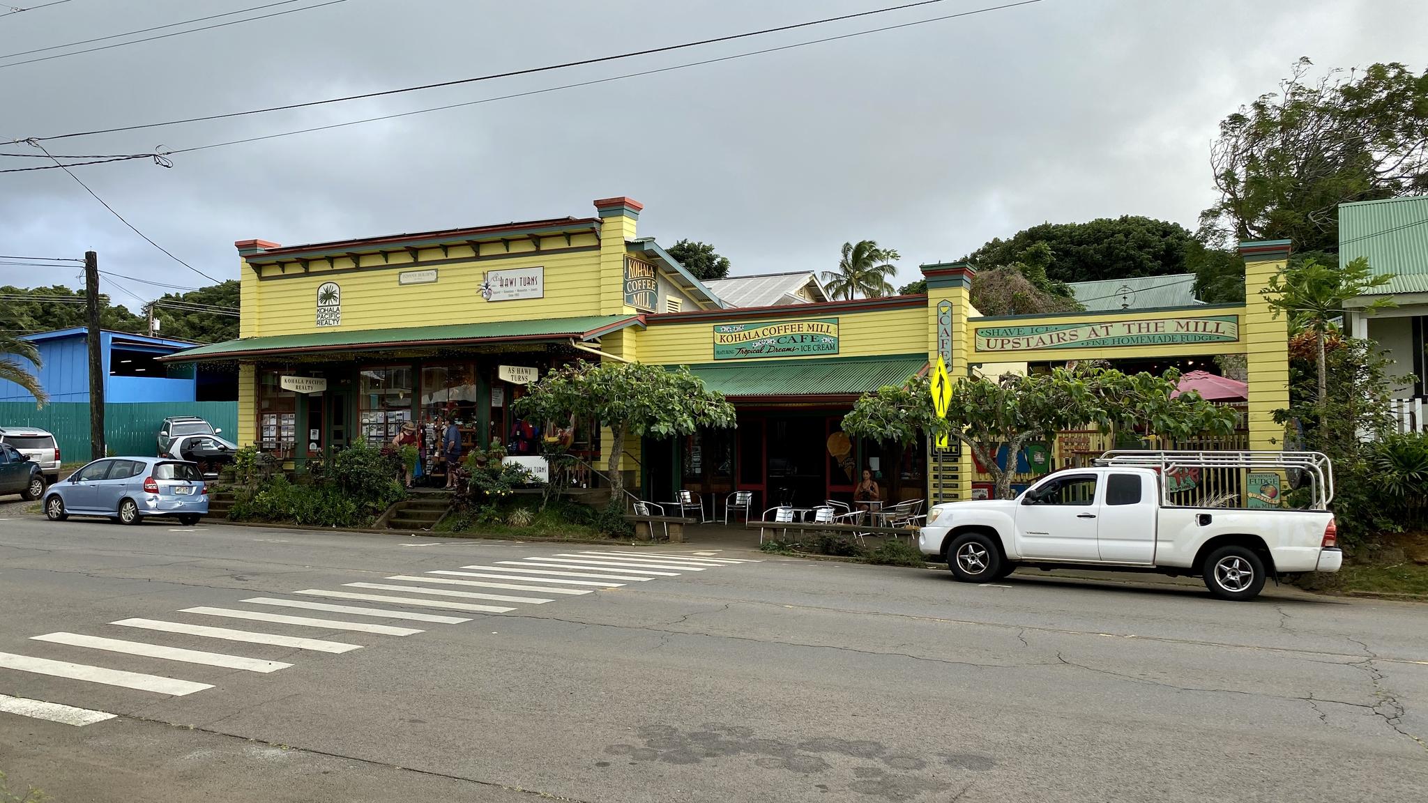 Yellow building with green awnings, cars parked on a street under an overcast sky.