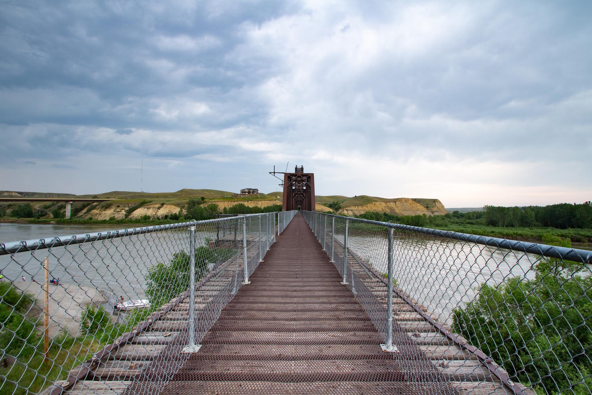 Long wooden and metal bridge over a river under a cloudy sky.