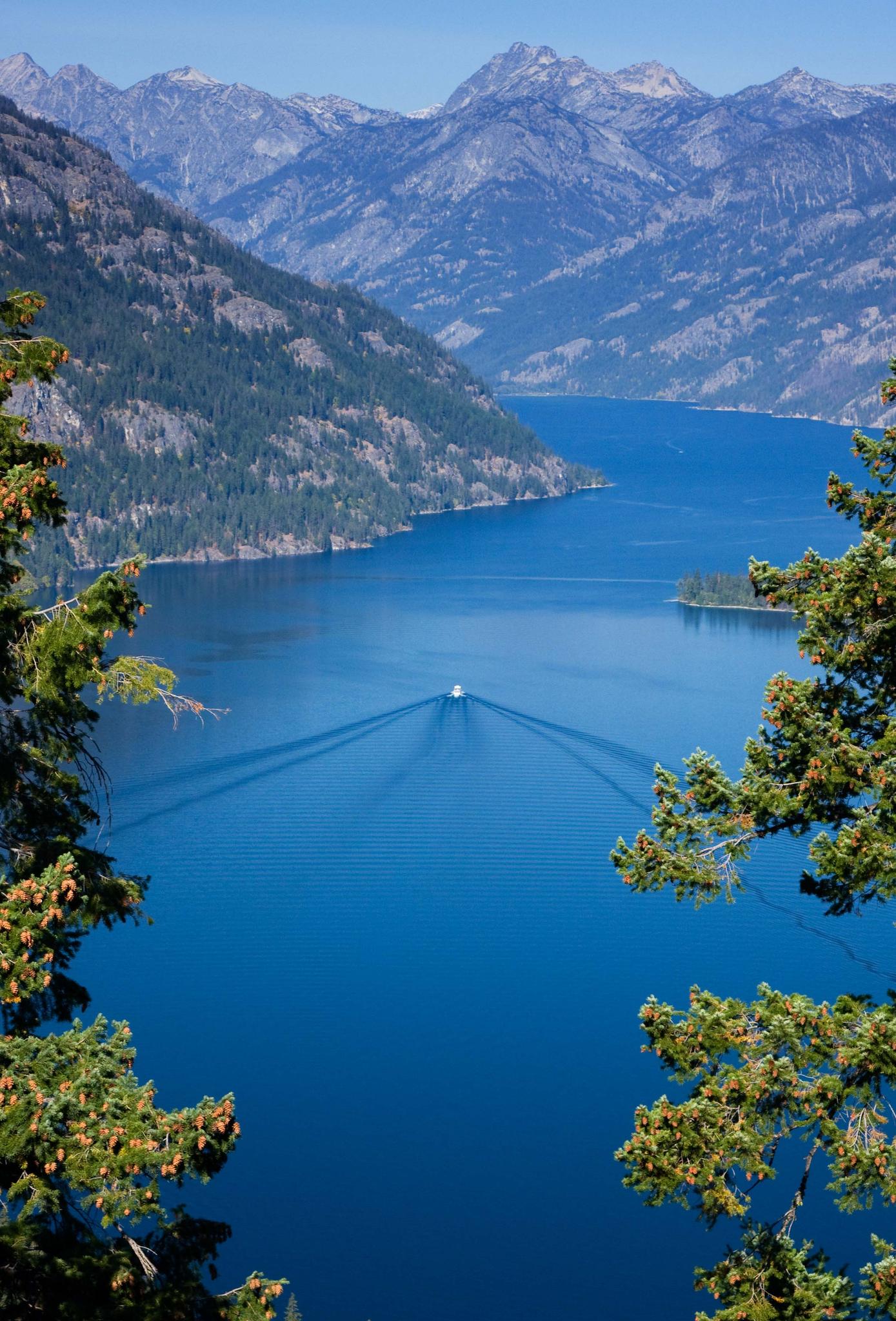 A boat on a blue lake, framed by mountains and trees, under bright sun.