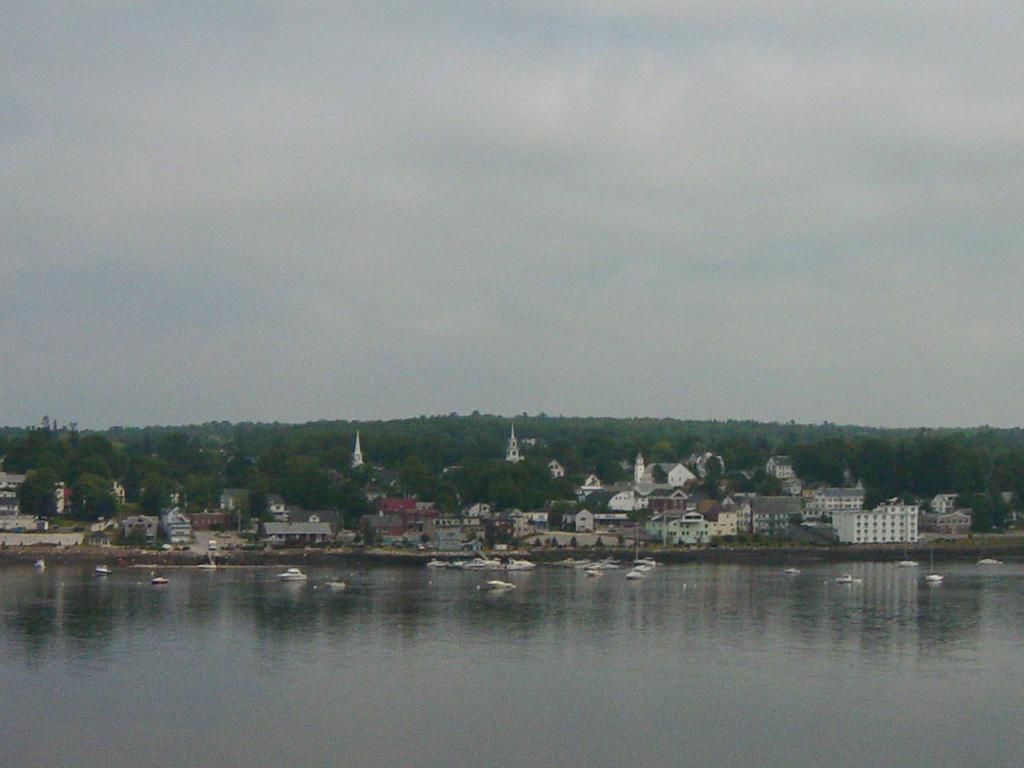 Coastal town with buildings and boats across water under an overcast sky.