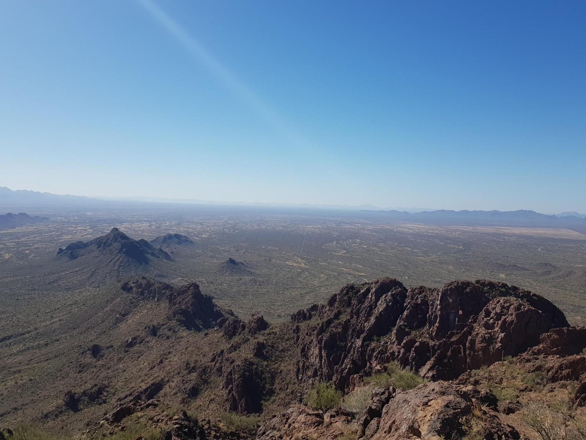 Expansive desert valley and distant mountains seen from a rocky peak.