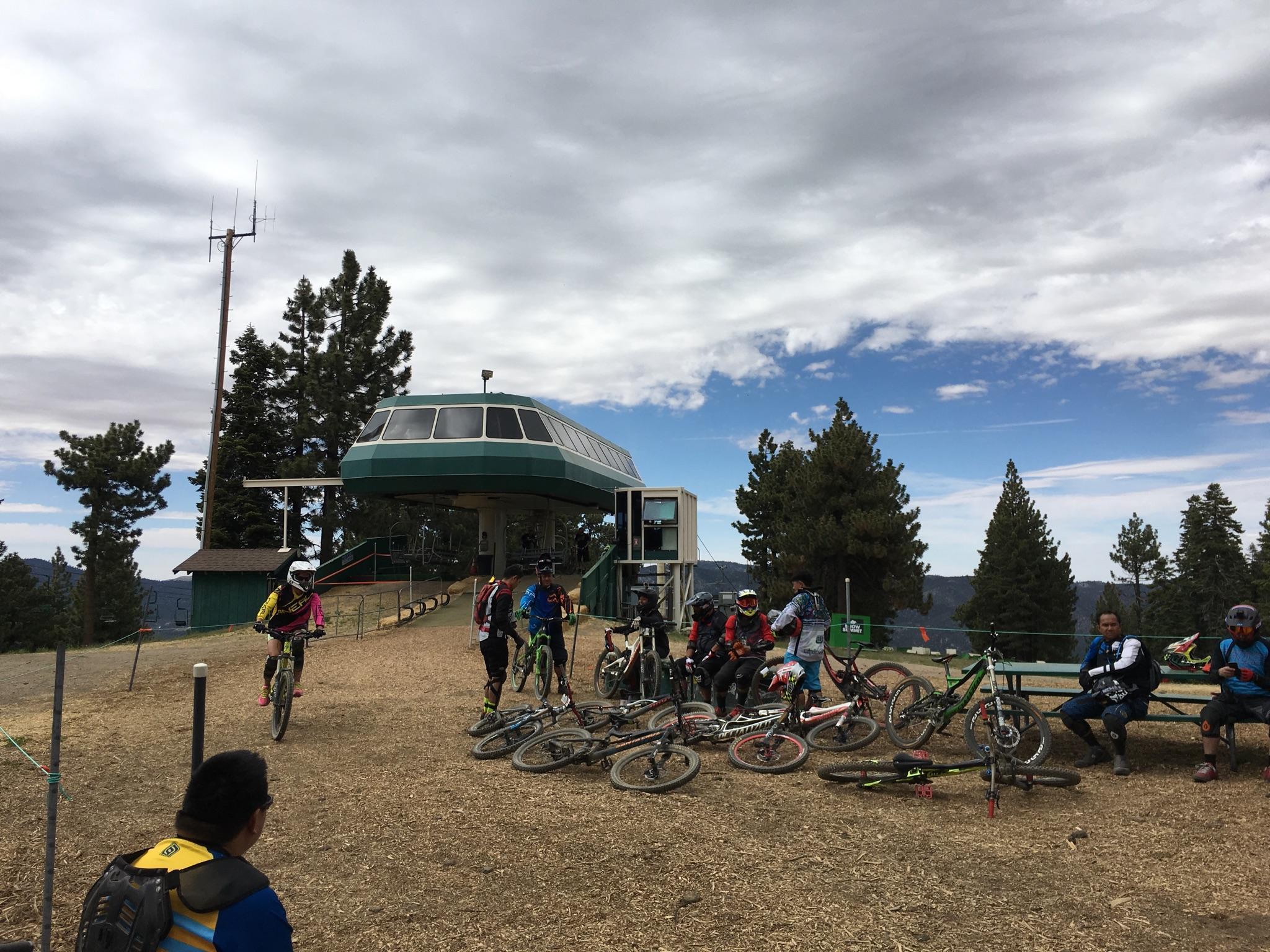 A group of mountain bikers gather near a ski lift under a partly cloudy sky.