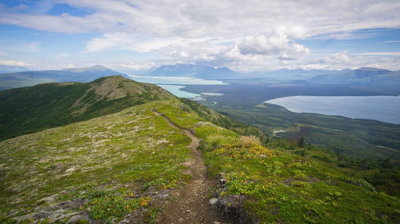 A narrow trail on a green mountain ridge overlooking vast lakes.