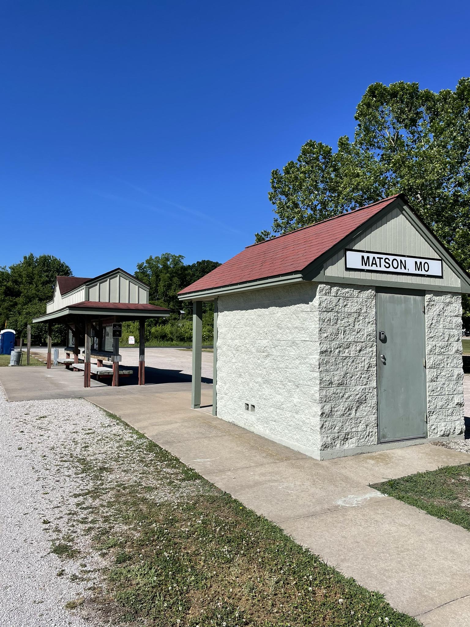 A small stone building and a covered shelter under a clear blue sky.