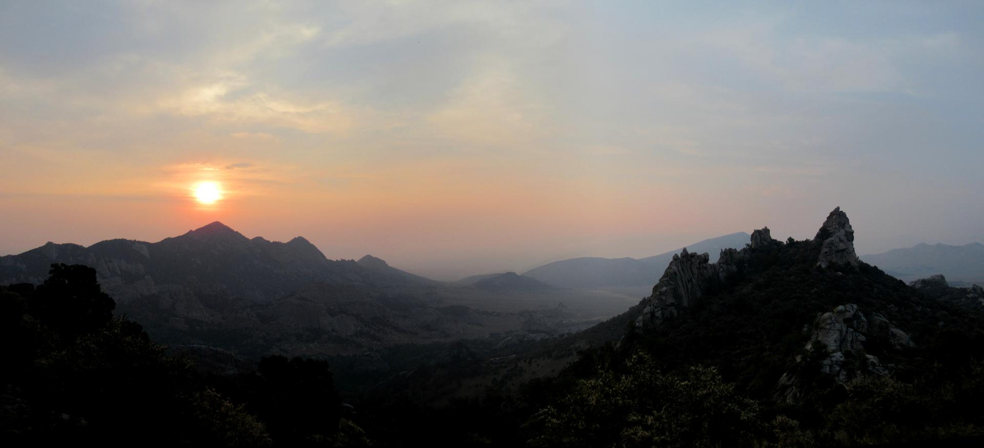 Hazy sunset over dark mountain peaks, with a bright orange sun.