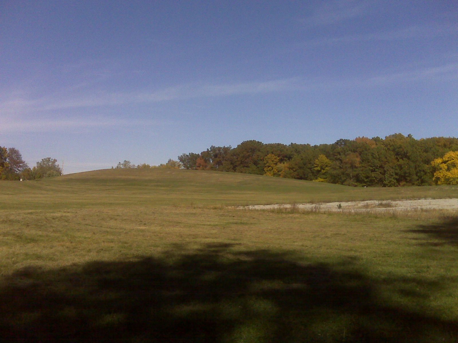 Sunny field with a grassy hill, distant autumn trees, and a small pond. - Franke Park East Loop