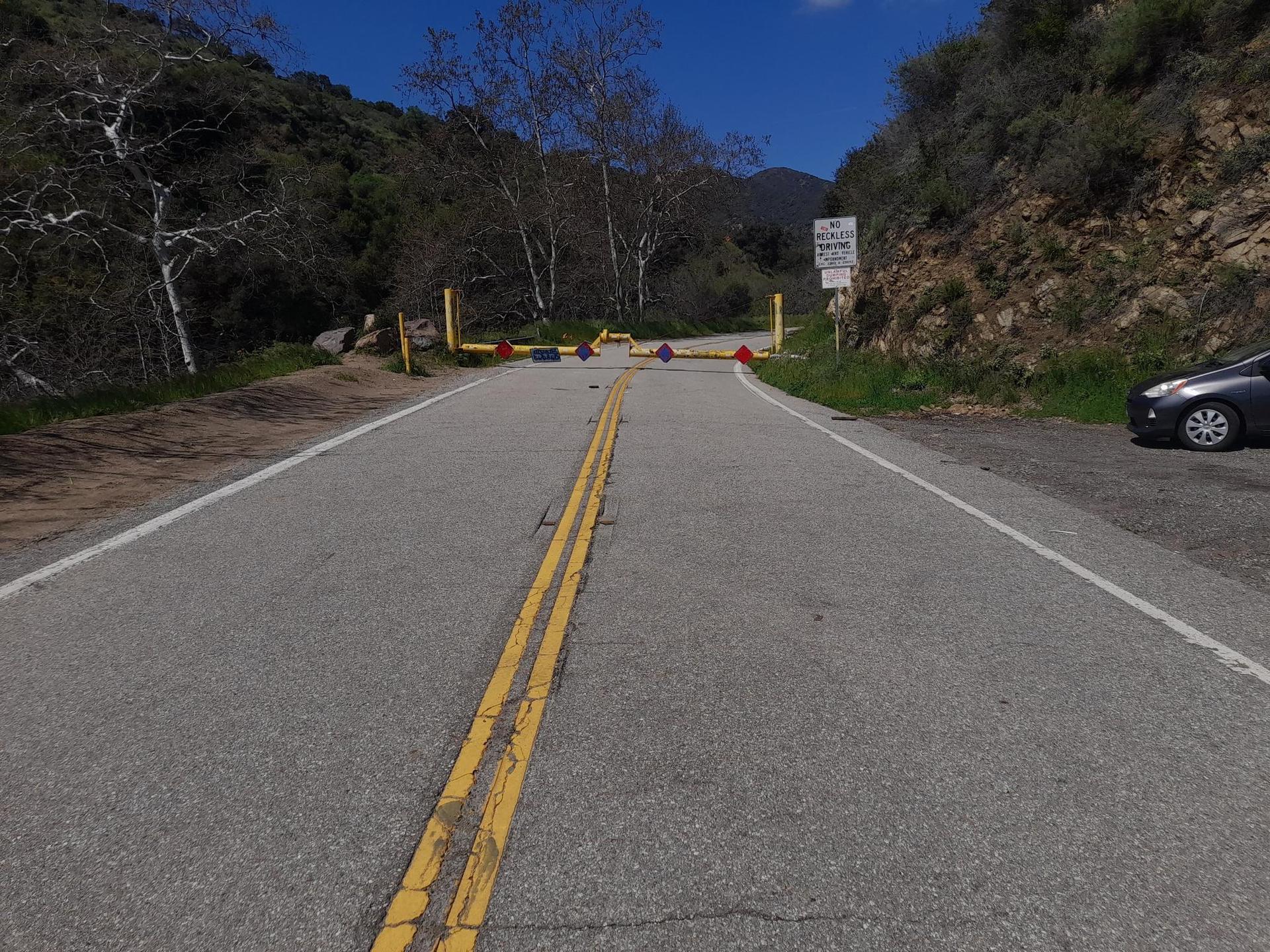 A paved road blocked by yellow gates, with a car parked on the side.