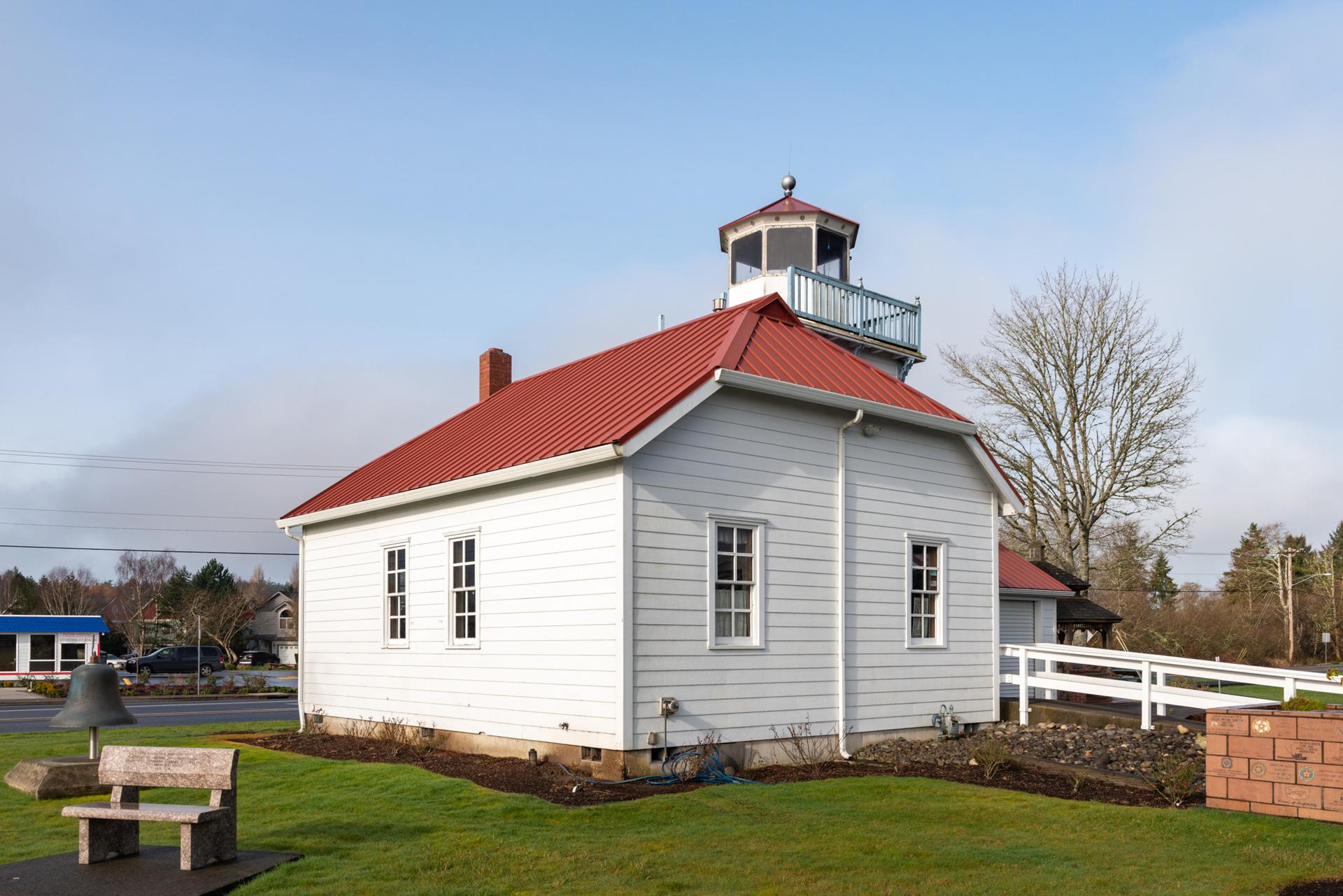 A small white building with a red roof and cupola on a sunny day.