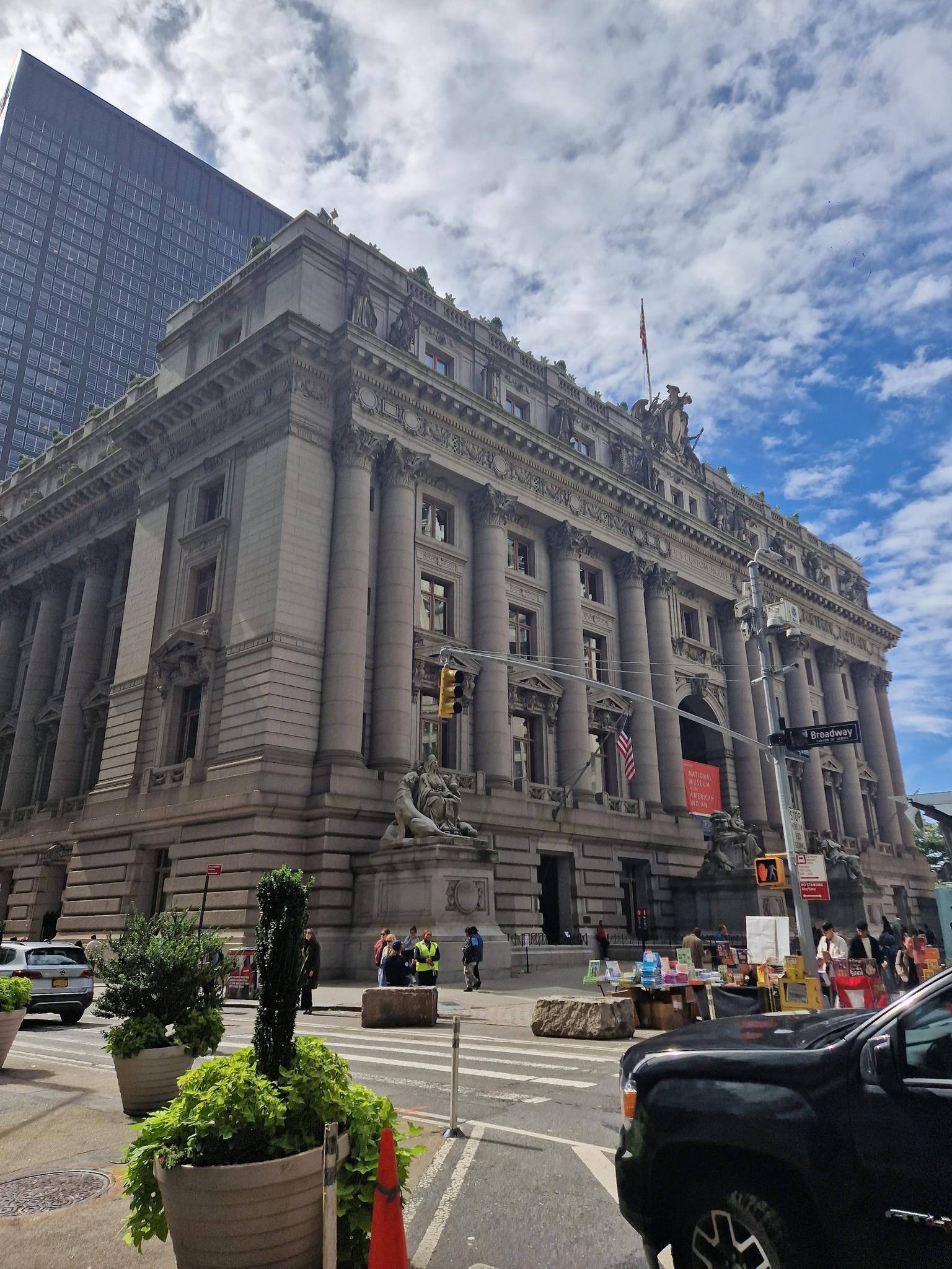 Ornate stone building with columns, flags, and people on a city street.