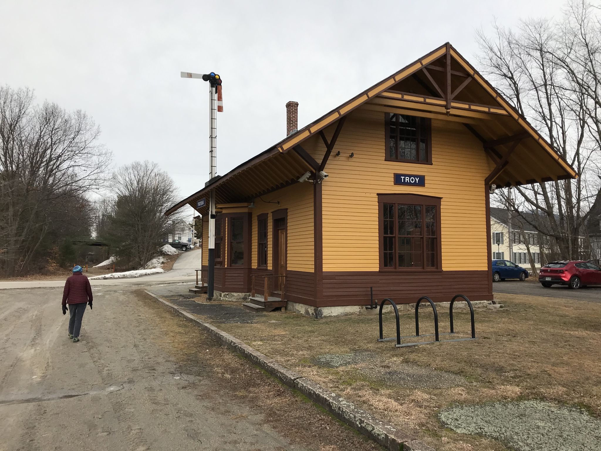 A person walks past a yellow and brown building on an overcast day. - Cheshire Recreational Rail Trail