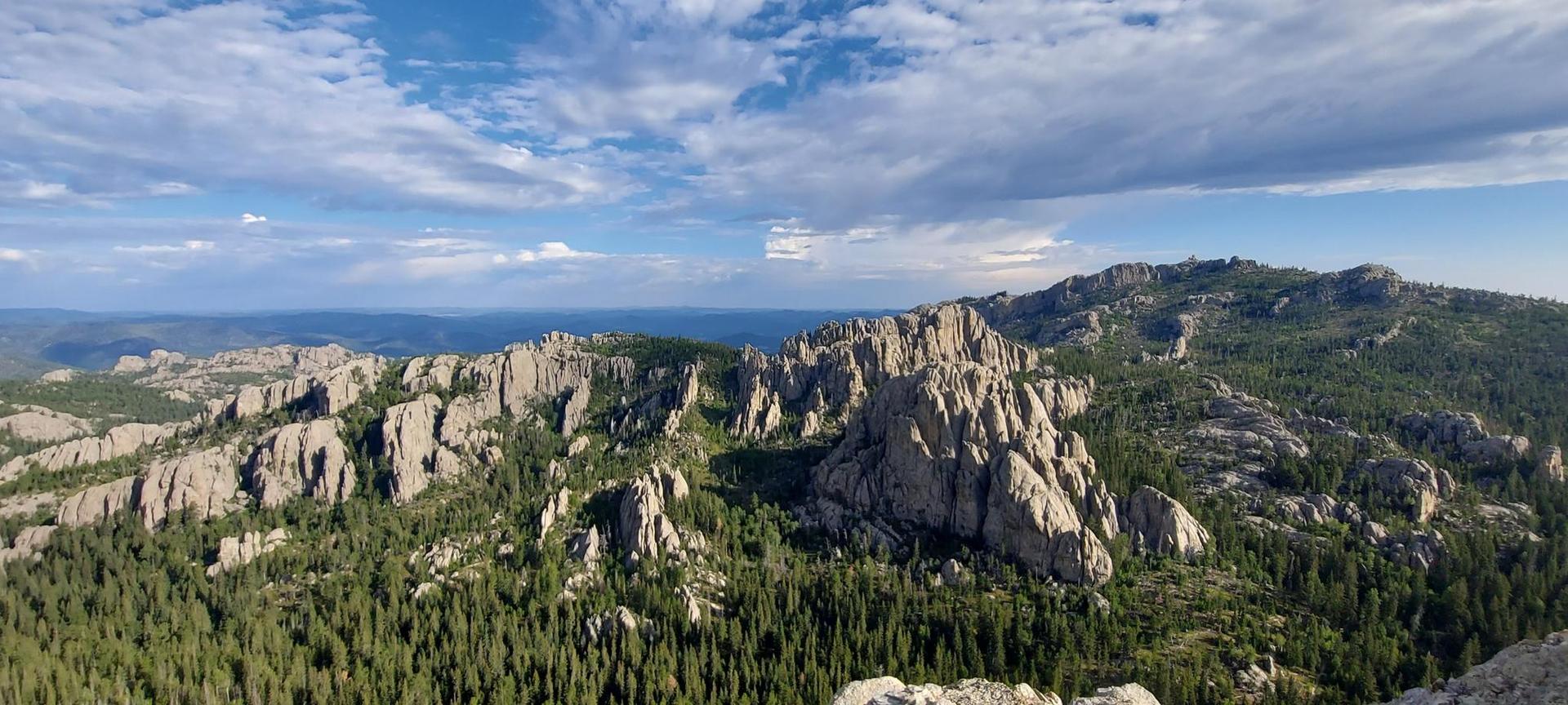 Panoramic view of rugged rock formations and dense green forests under a partly cloudy sky.