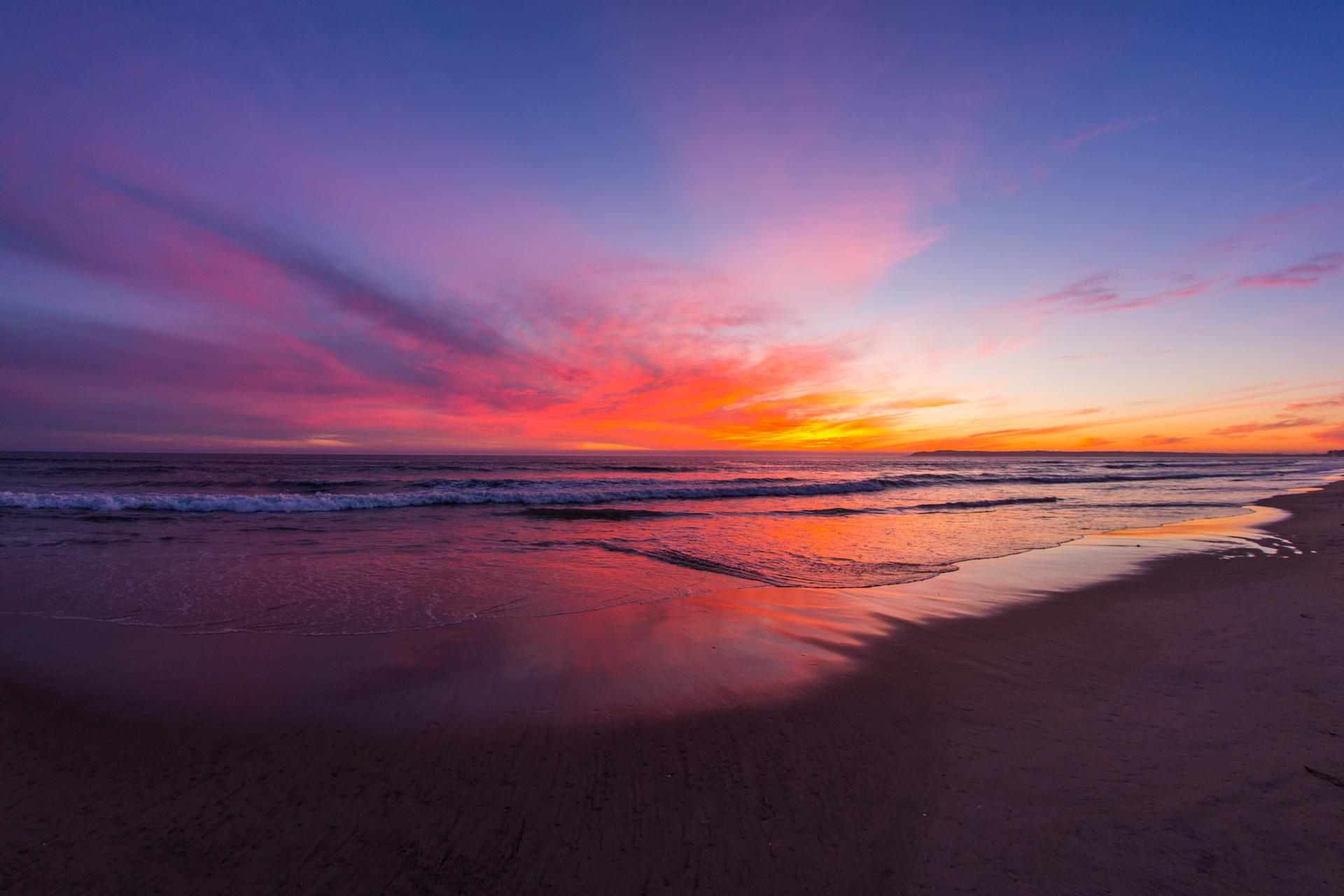 Vibrant sunset over ocean beach, colorful clouds reflecting on wet sand.
