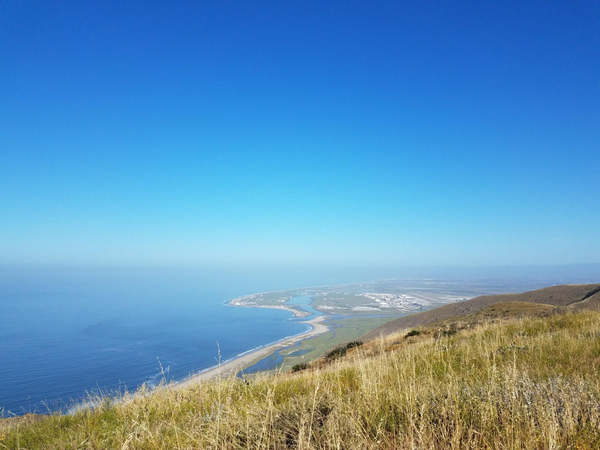 Expansive view of a blue ocean and coastline from a grassy hill.