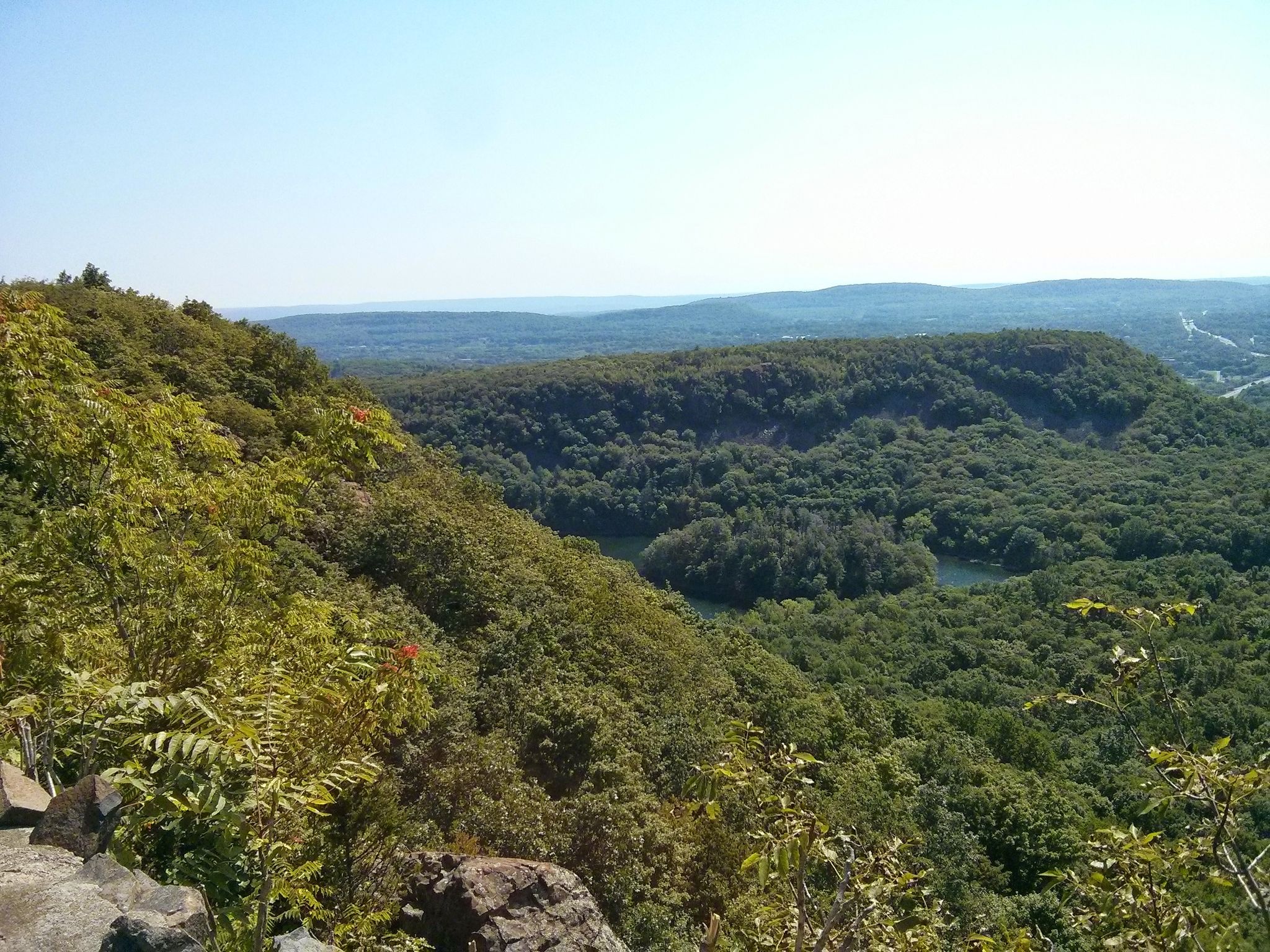Panoramic view of a lush green forested valley with a small lake under clear skies. - Ragged Mountain Blue Trail Loop