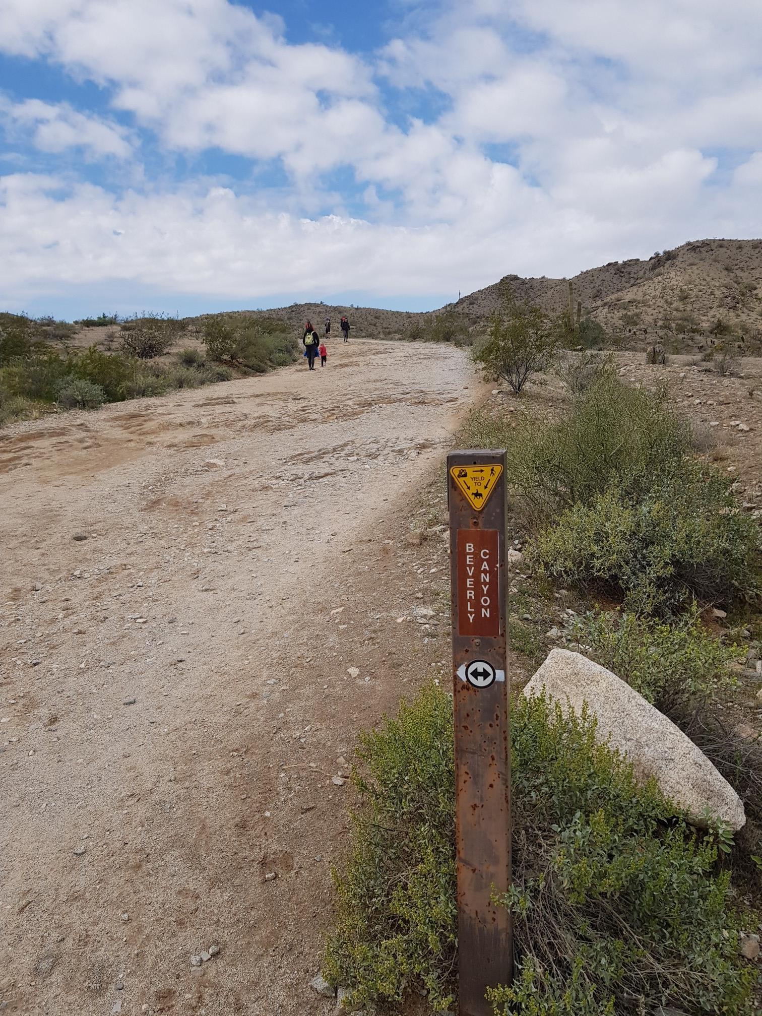 Dirt trail with a marker, people walking in the arid landscape.