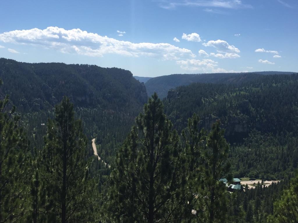 A wide view of a forested valley with distant mountains under a bright sky.