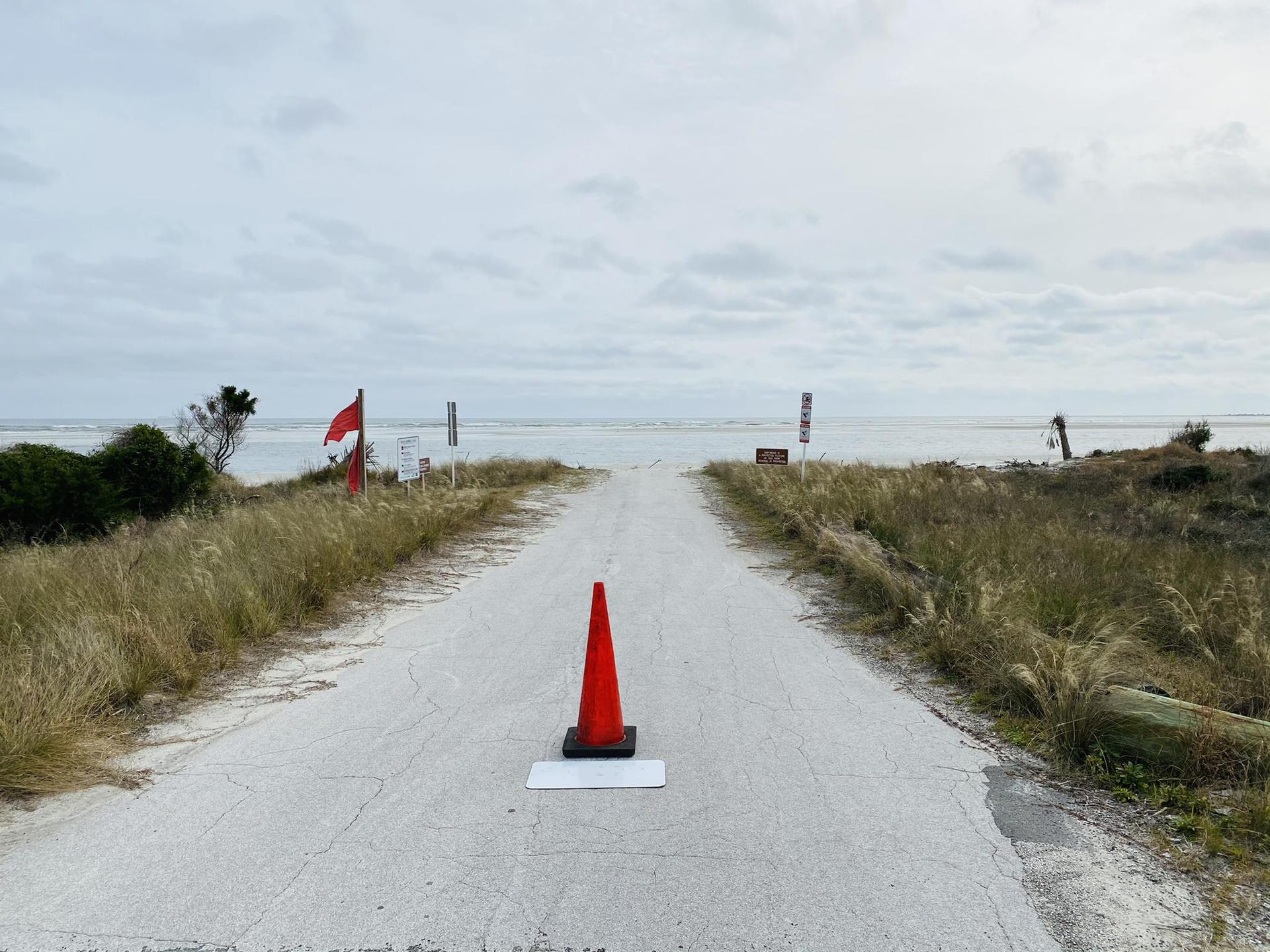 Overcast view of a paved road with an orange cone leading to water.