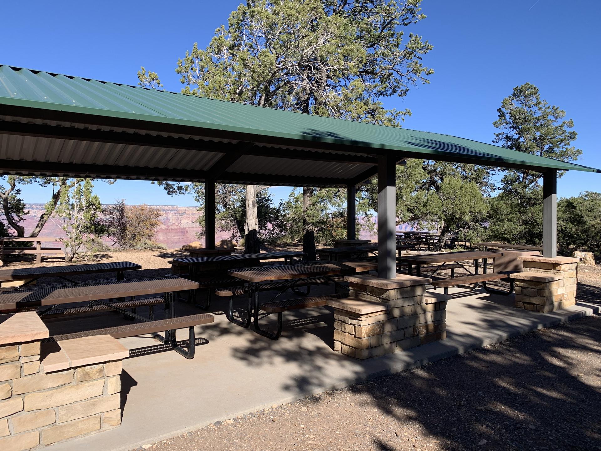 Covered outdoor picnic area with multiple tables and benches on a sunny day.