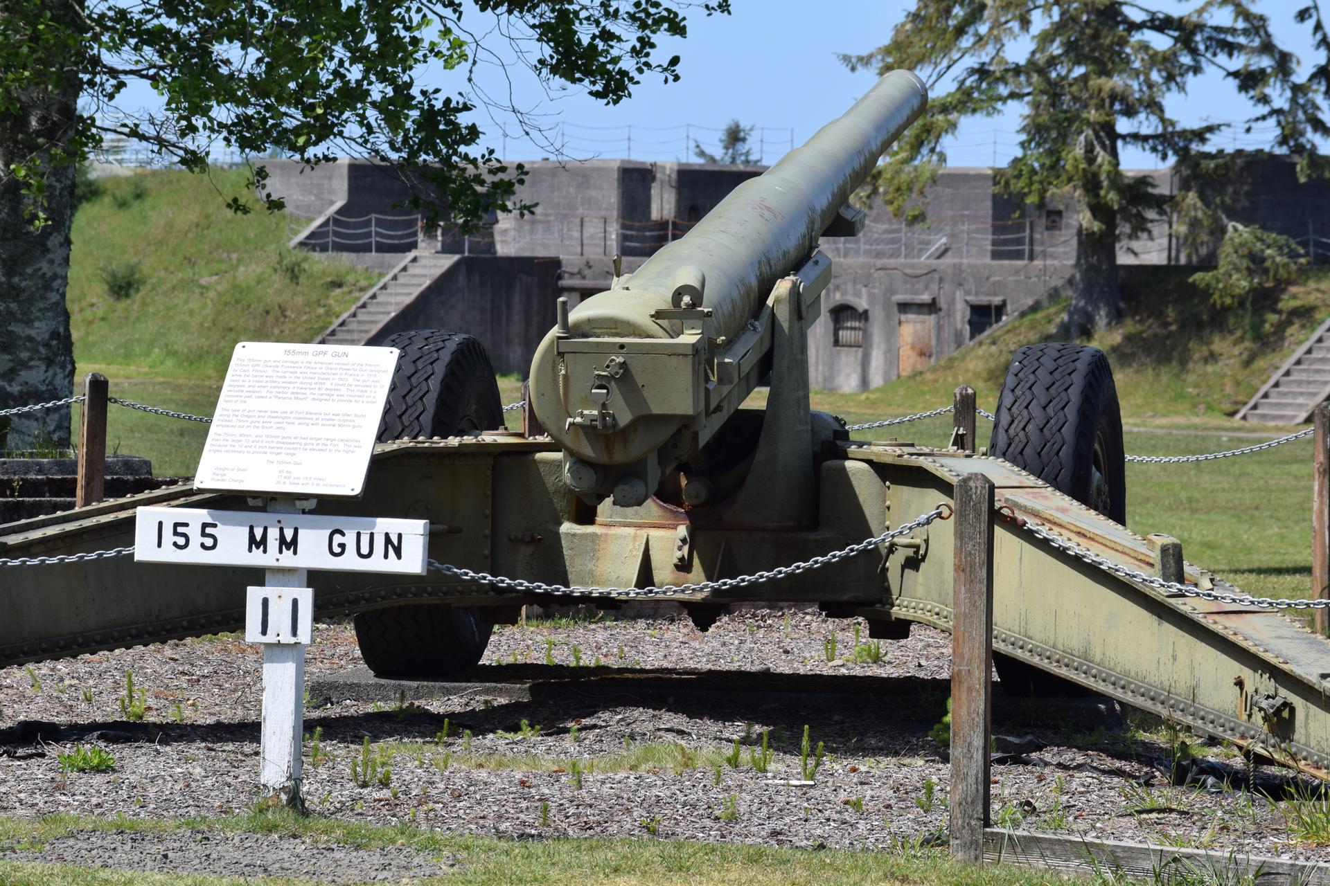 A large green military gun on display in a sunny park.