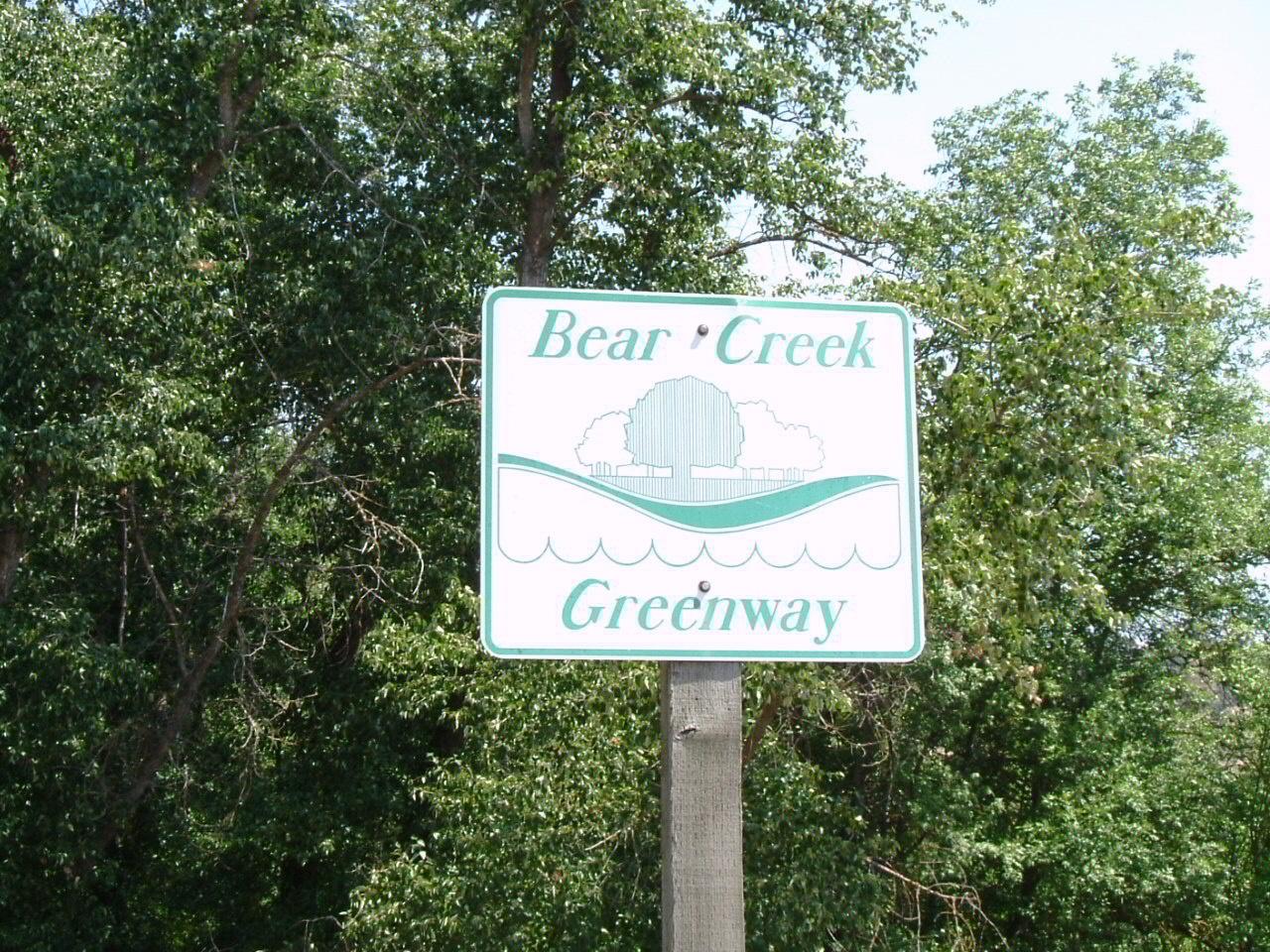 A white and green sign on a wooden post against lush green trees.