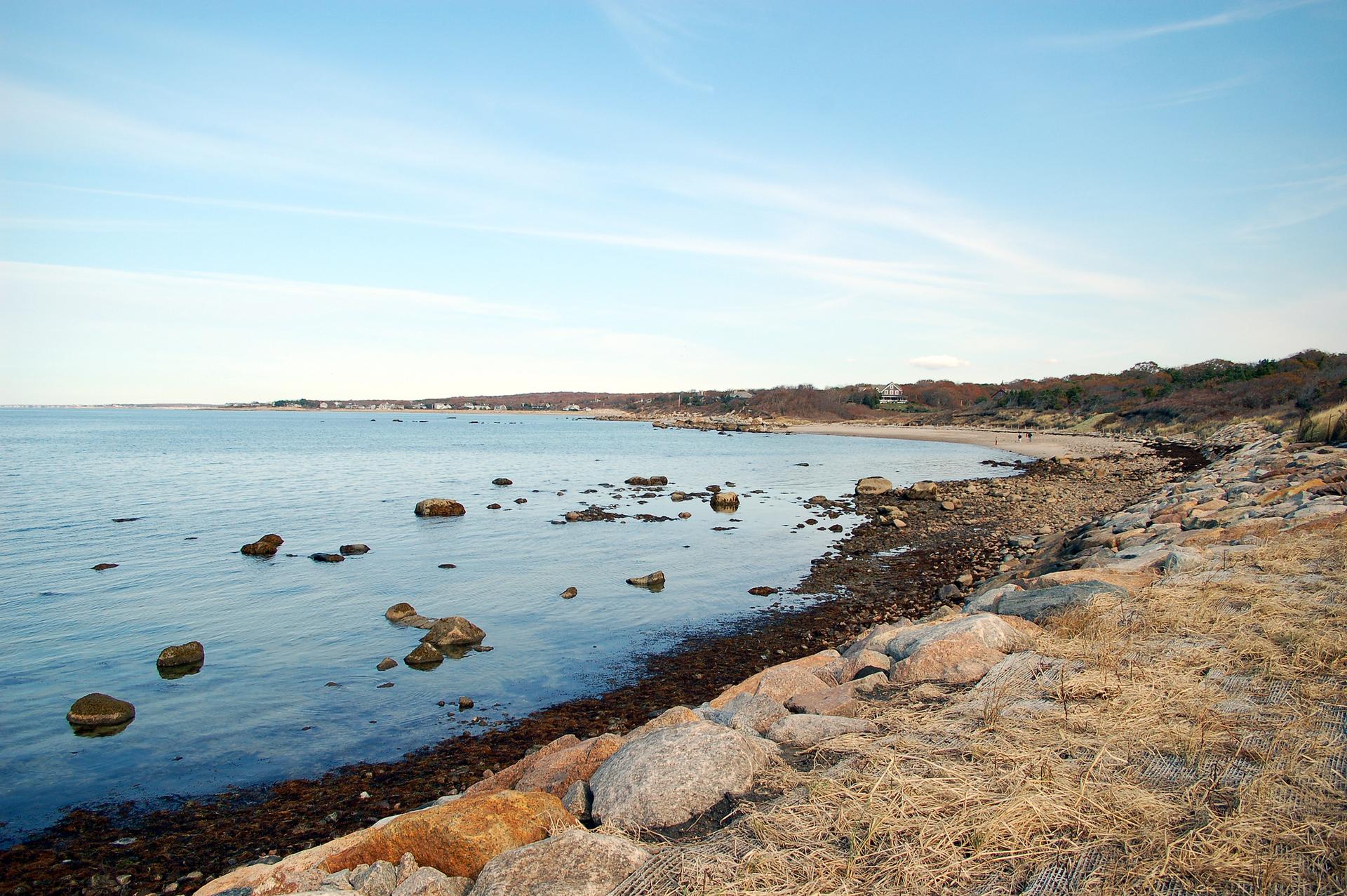 Wide view of a rocky beach with calm water under a clear blue sky.