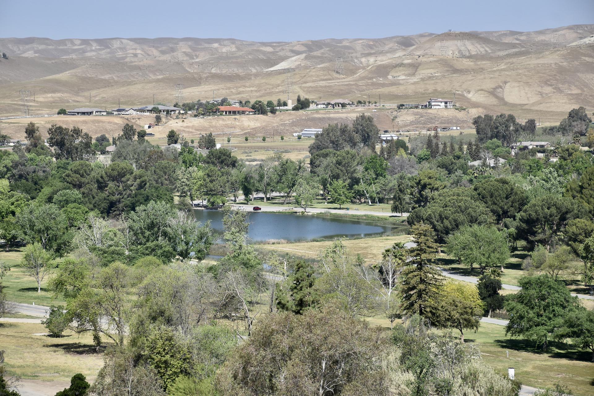 An aerial view of a small lake surrounded by green trees and dry hills.