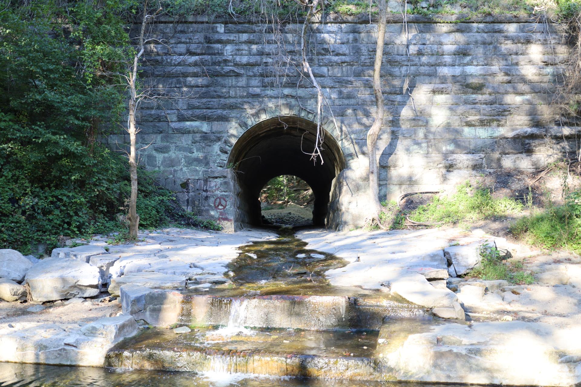 Water flows from a dark stone tunnel into a rocky stream bed.