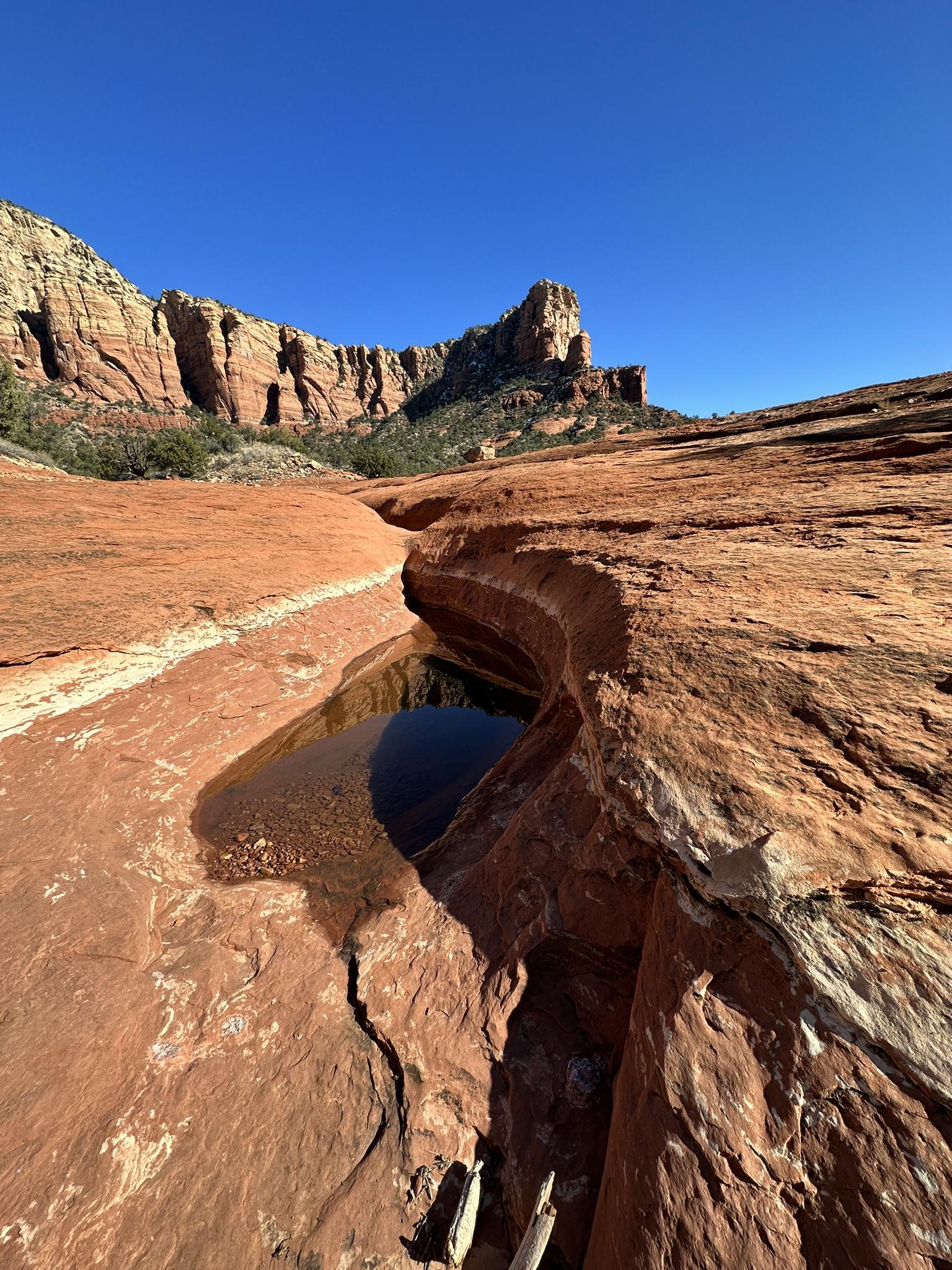 Clear water pools in a narrow crevice of sunlit red rock formations.