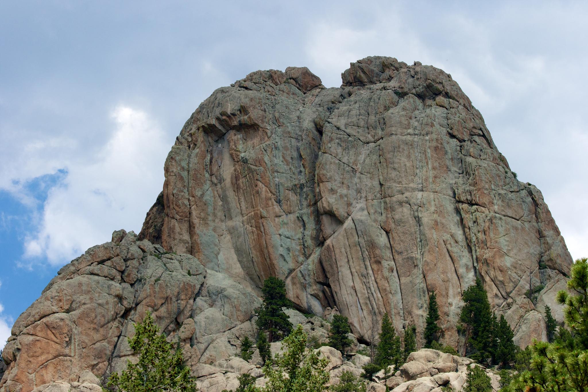 Towering, textured rock formation with sparse trees against a cloudy sky.