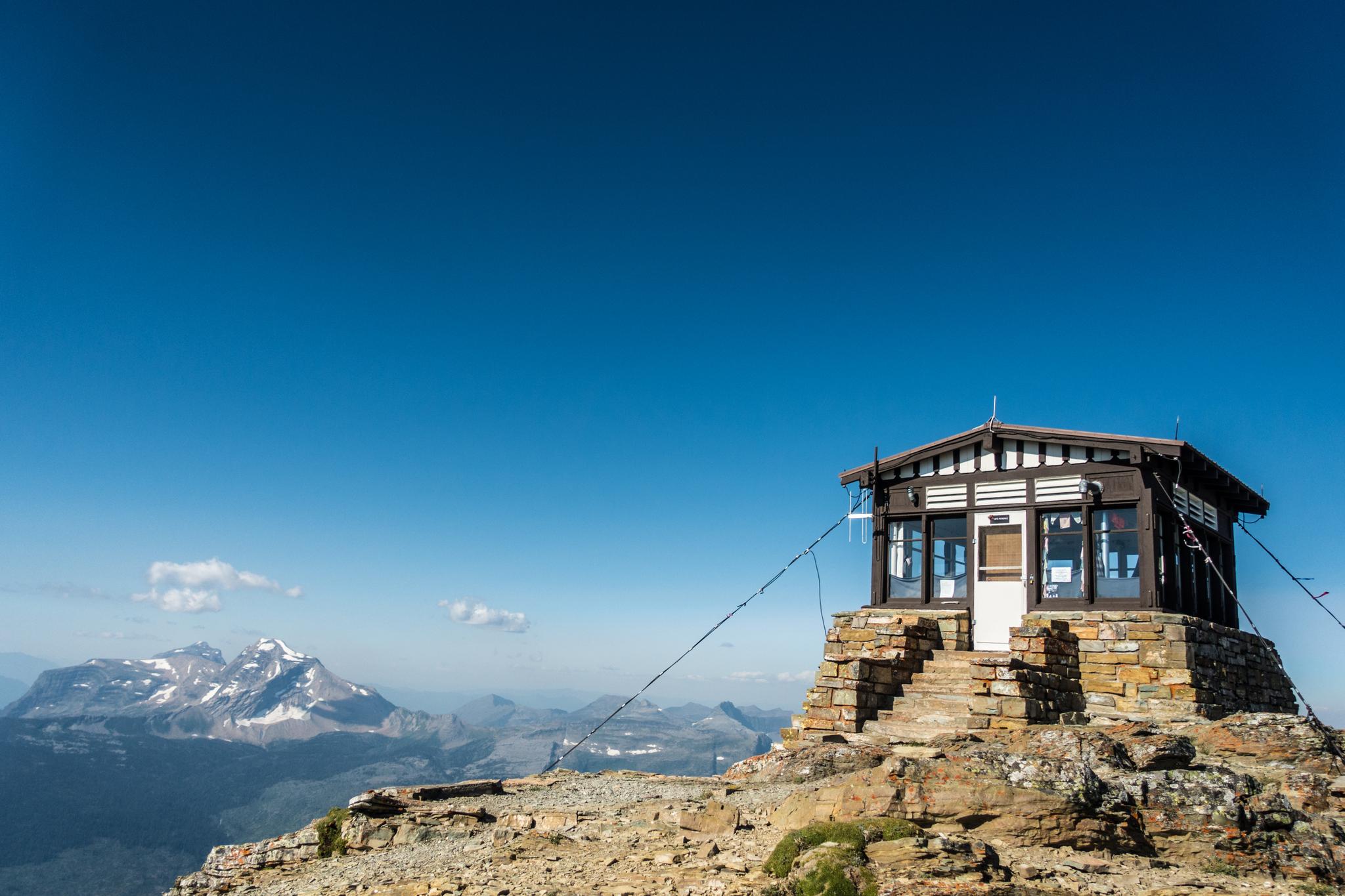A small building on a rocky peak overlooks a vast mountain landscape.