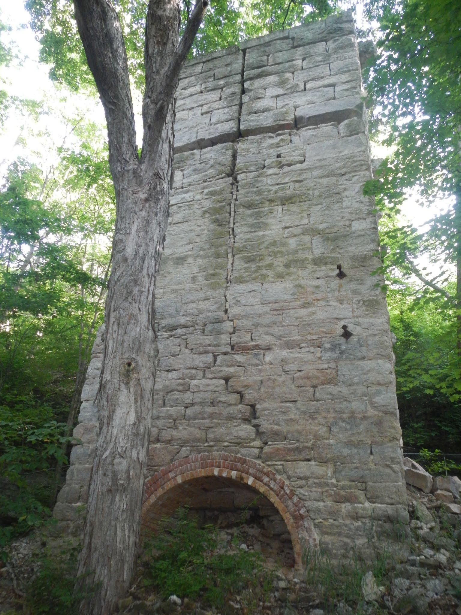 Tall stone structure with brick arch next to a large tree in dappled light.