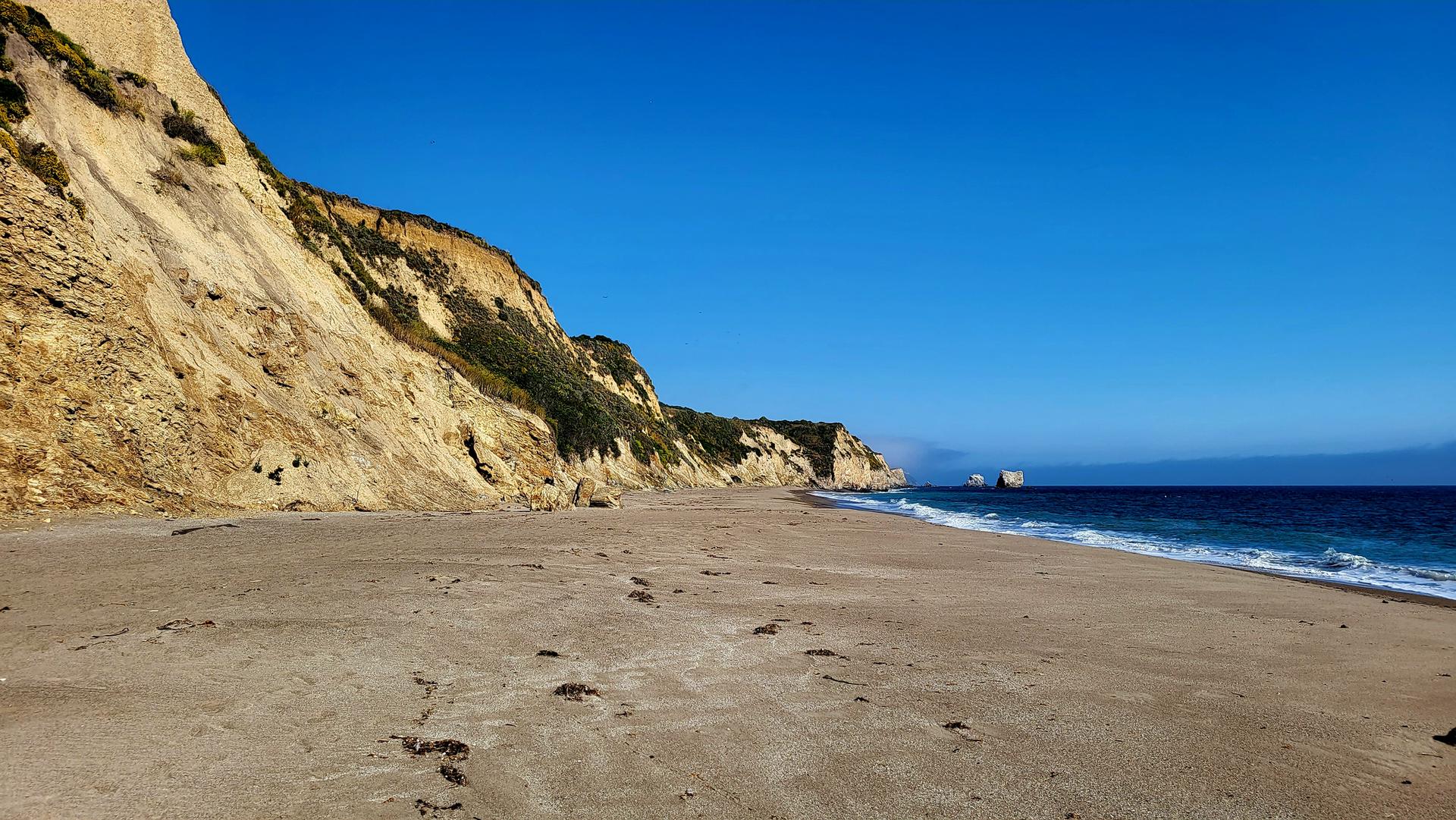 Wide sandy beach next to towering cliffs under a clear blue sky.