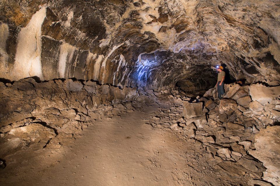 Person with headlamp exploring a dark, rocky cave with a dirt path. - Dead Horse to Tea Kettle Cave