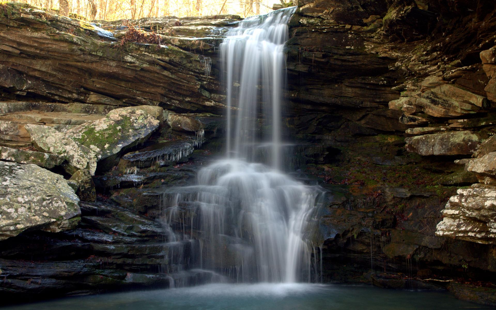 A beautiful waterfall cascades over rocky cliffs into a clear pool.