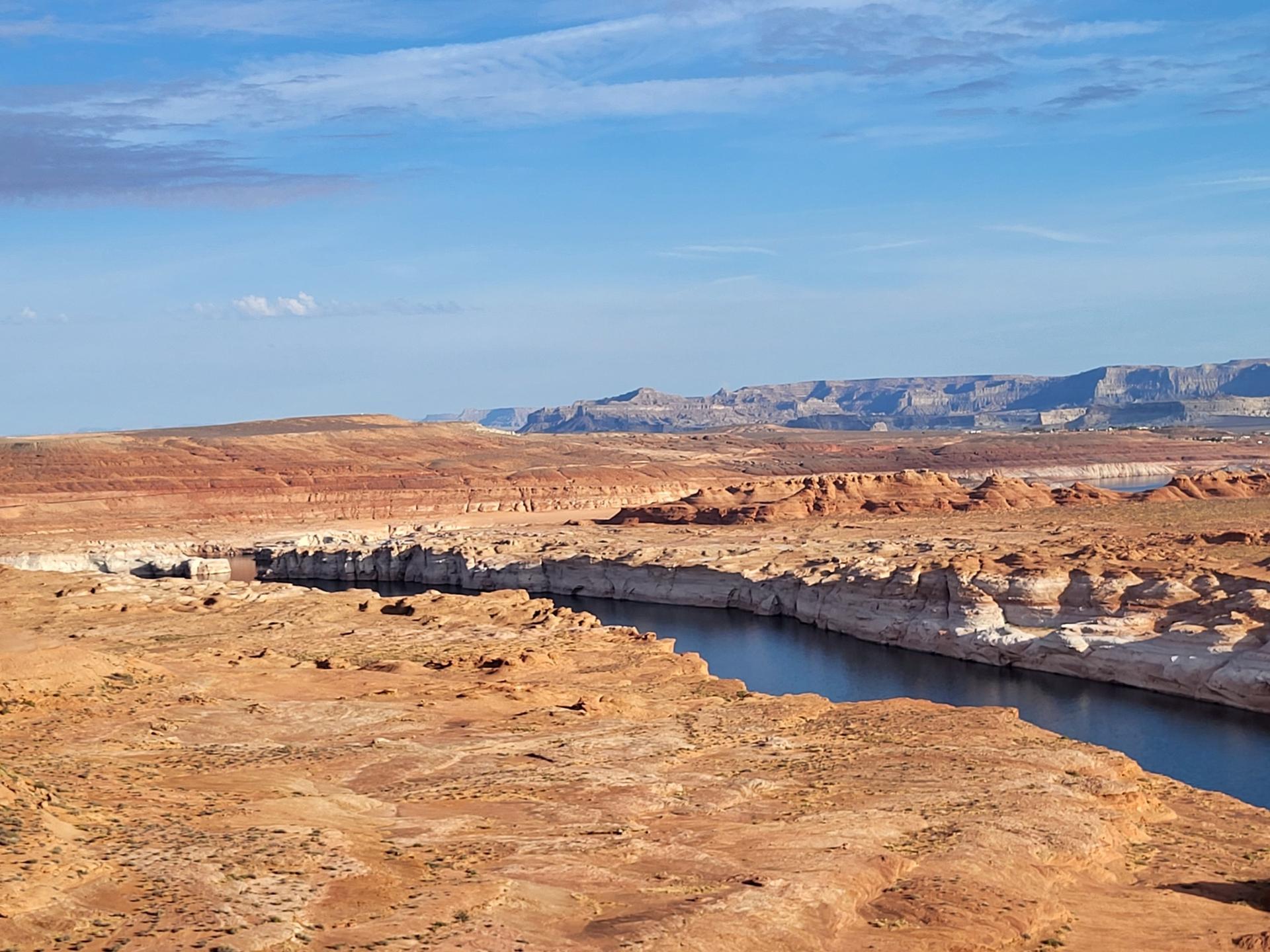 A winding river cuts through a vast, arid canyon under a bright sky.